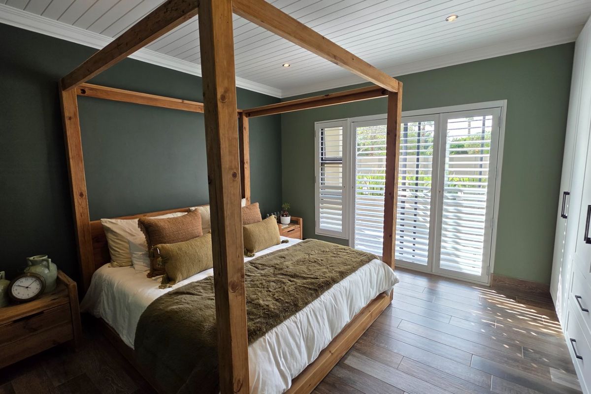 A well-appointed bedroom featuring timber-look tile flooring, built-in wardrobes, plantation shutters, and direct access to the outdoors through french doors.