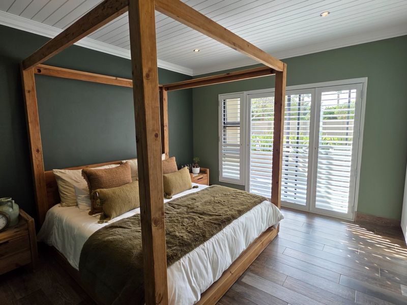 A well-appointed bedroom featuring timber-look tile flooring, built-in wardrobes, plantation shutters, and direct access to the outdoors through french doors.