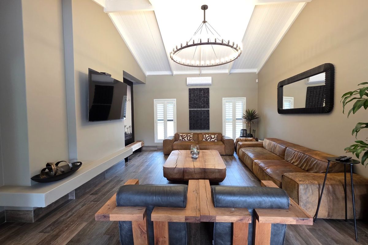 Spacious living room featuring a high vaulted ceiling with exposed beams, timber-look tile flooring, and plantation shutters, creating a bright and modern atmosphere.