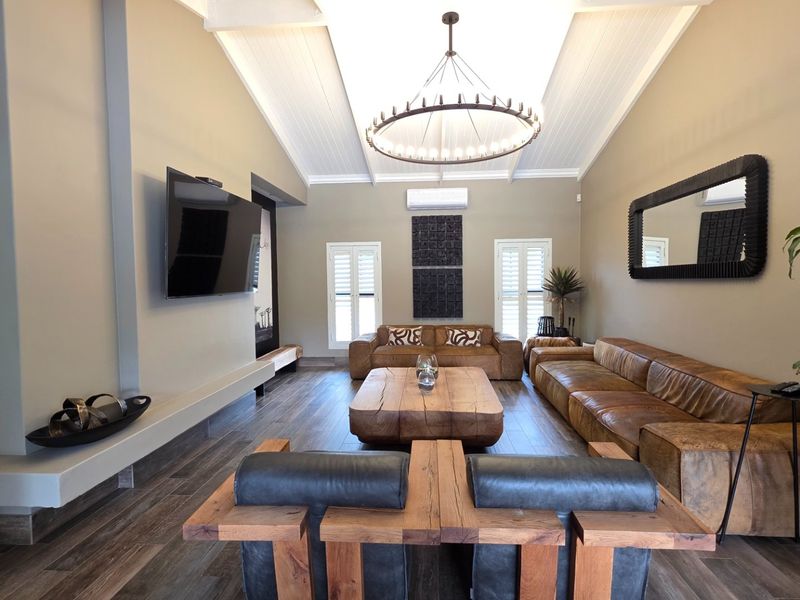 Spacious living room featuring a high vaulted ceiling with exposed beams, timber-look tile flooring, and plantation shutters, creating a bright and modern atmosphere.