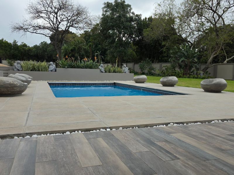 A well-maintained outdoor pool area featuring a paved deck, timber flooring, and a landscaped garden with a perimeter wall.