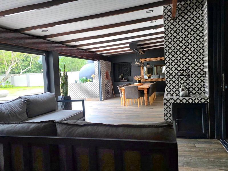Spacious covered patio featuring exposed timber beams, wood-look flooring, and a striking tiled feature wall with a built-in fireplace, perfect for outdoor entertaining.