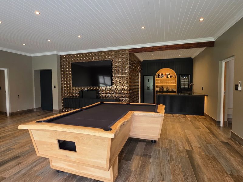 A sophisticated entertainment room featuring a custom built-in bar with integrated wine storage, decorative metallic wall accents, and high-quality timber-look tile flooring.