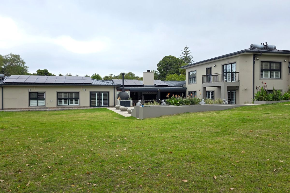 Rear view of a modern two-story house featuring solar panels, a spacious lawn, an outdoor fireplace, and a balcony.