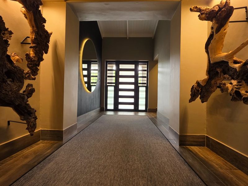 A well-lit, modern entrance hall featuring tiled flooring, a striking backlit circular mirror, and a contemporary timber-framed front door.