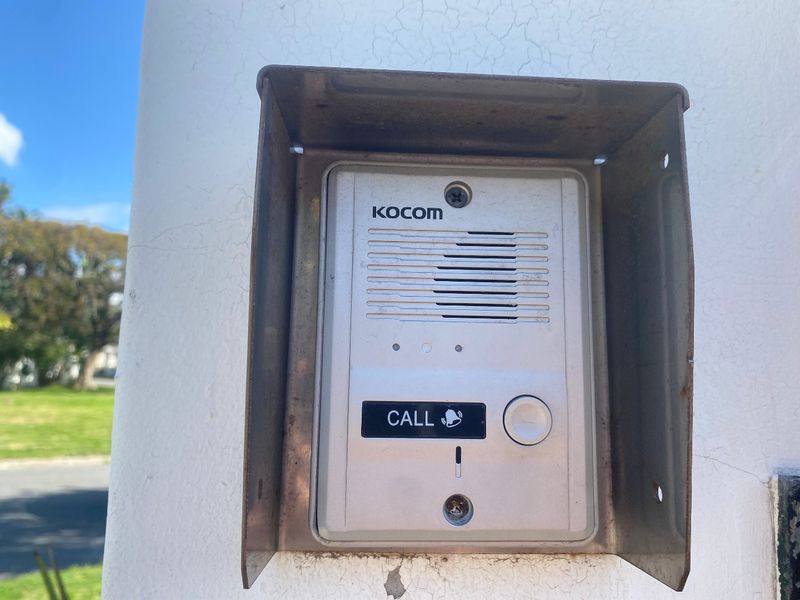A close-up view of a Kocom intercom system mounted on an exterior wall with visible weathering and cracking to the surrounding masonry.