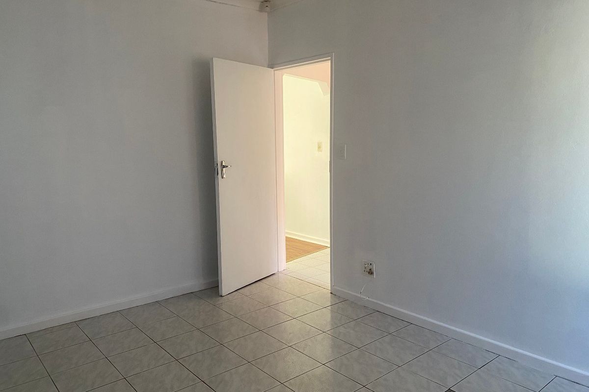 An empty room featuring neutral tiled flooring and a white interior door, providing a blank canvas for potential bedroom or office use.