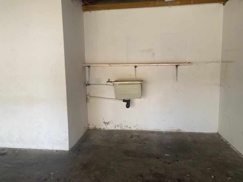 A basic utility space featuring a wall-mounted sink, exposed plumbing, and a storage shelf, requiring maintenance and cosmetic updates.