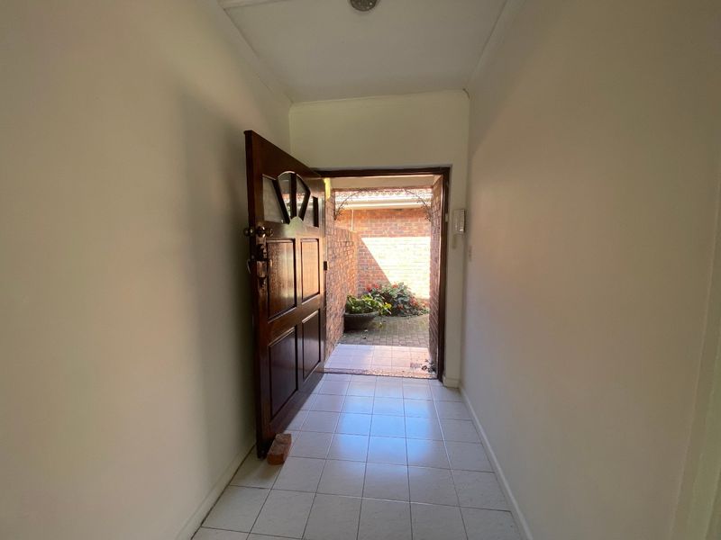 A bright entrance hallway featuring tiled flooring and a solid timber front door leading to an outdoor courtyard area.