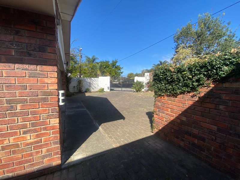 A view of the front entrance area featuring a paved driveway, brick boundary walls, and a secure metal gate.