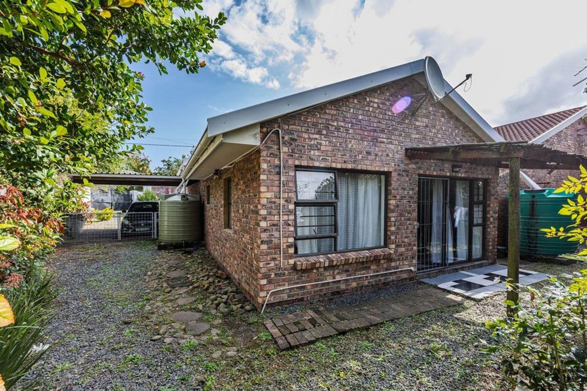 Rear view of a face brick house featuring a sliding door entrance, a small paved patio area, and an adjacent carport with a water tank.