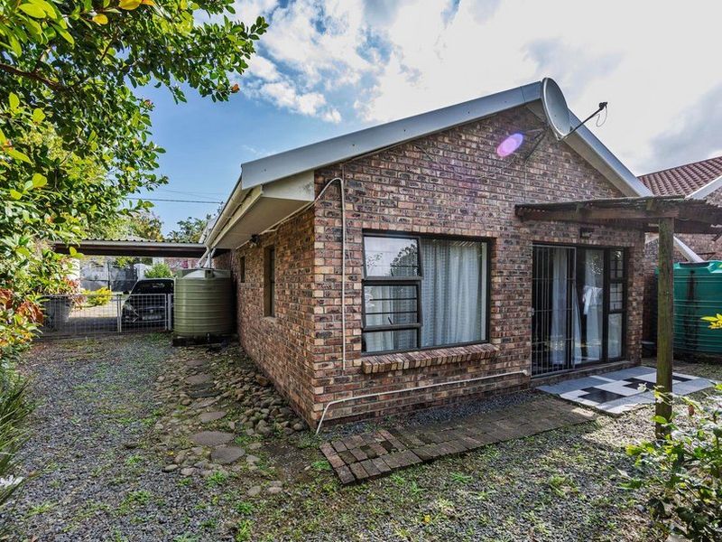 Rear view of a face brick house featuring a sliding door entrance, a small paved patio area, and an adjacent carport with a water tank.