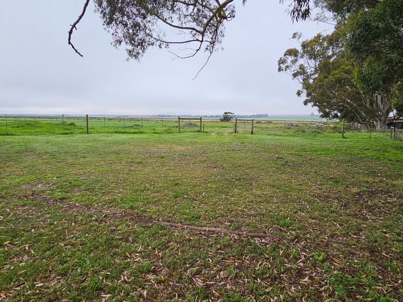 A spacious rear garden area featuring a paved patio, wire fencing, and mature trees, overlooking an expansive open field.