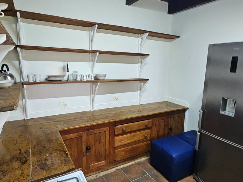 A functional scullery area featuring rustic wooden cabinetry, extensive open shelving, and durable tiled flooring, providing ample storage and prep space.