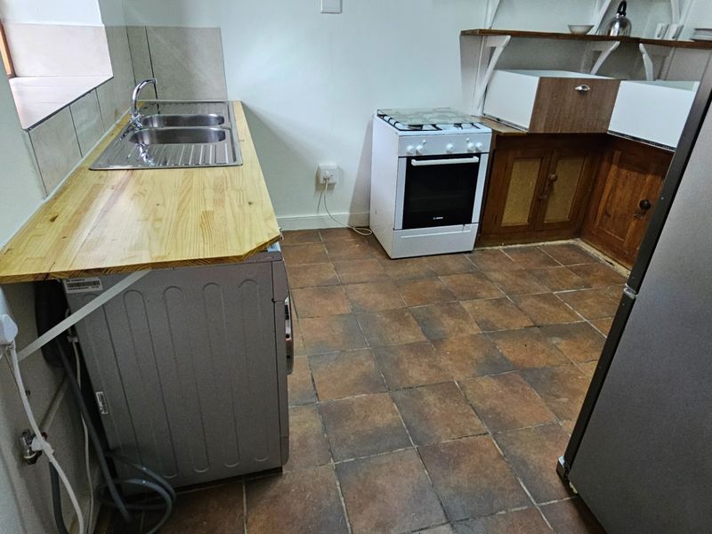 A functional scullery area featuring a double sink, wooden countertop, freestanding stove, and traditional wooden cabinetry with open shelving.