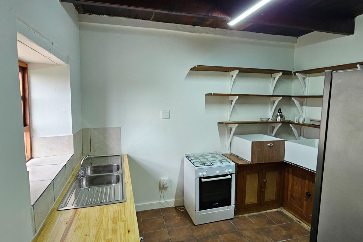 A rustic kitchen featuring exposed timber ceiling beams, open shelving, a double bowl sink, and a freestanding gas stove.