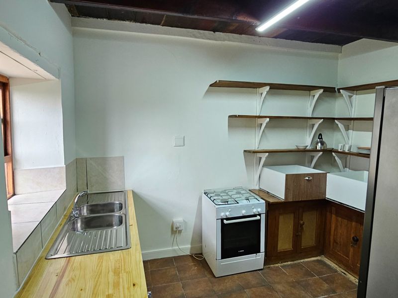 A rustic kitchen featuring exposed timber ceiling beams, open shelving, a double bowl sink, and a freestanding gas stove.