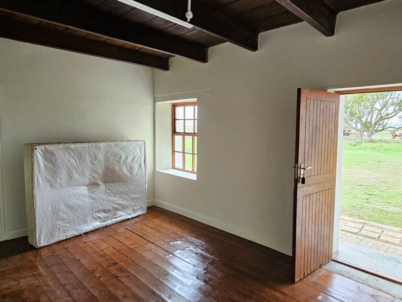 A rustic bedroom featuring polished timber flooring, exposed ceiling beams, and direct access to the garden through a timber door.