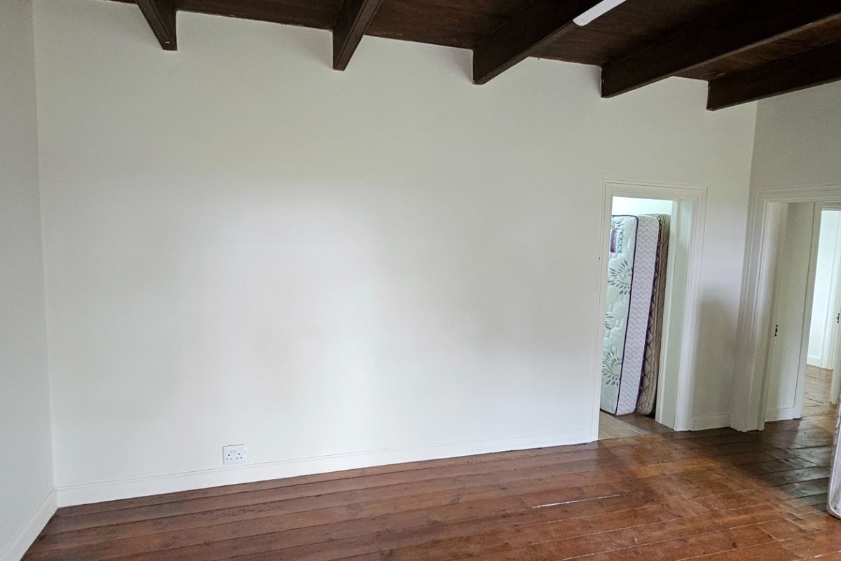 An empty bedroom featuring exposed timber ceiling beams and original timber floorboards, offering a blank canvas for renovation or interior design.