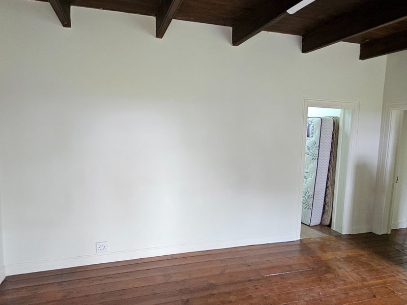 An empty bedroom featuring exposed timber ceiling beams and original timber floorboards, offering a blank canvas for renovation or interior design.