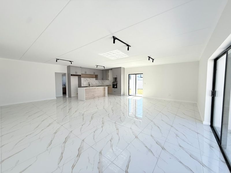 Spacious open-plan living area featuring modern kitchen cabinetry, a central island, and high-gloss marble-look floor tiles with large sliding doors to the exterior.