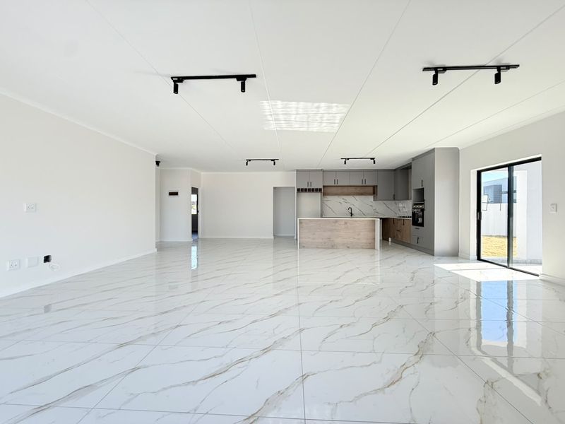 Spacious open-plan living and kitchen area featuring modern marble-look floor tiles, sleek built-in cabinetry, and direct access to the outdoor space.