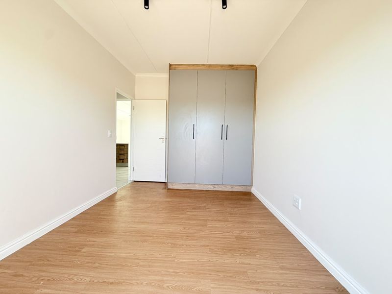 A bright, empty bedroom featuring modern laminate flooring and neutral walls, complete with built-in grey cabinetry for storage.