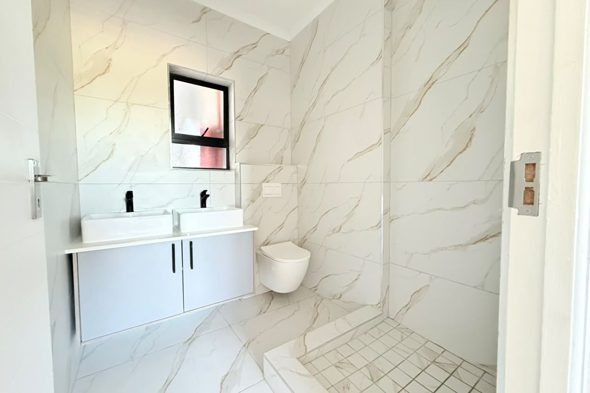 Modern bathroom featuring a double vanity, wall-mounted toilet, and a spacious walk-in shower with elegant marble-look tiling and contemporary black matte fixtures.