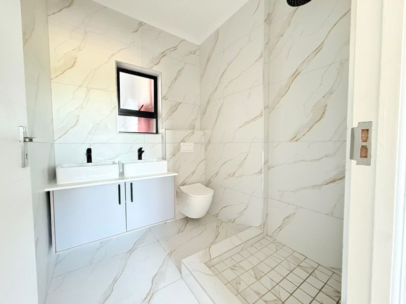 Modern bathroom featuring a double vanity, wall-mounted toilet, and a spacious walk-in shower with elegant marble-look tiling and contemporary black matte fixtures.