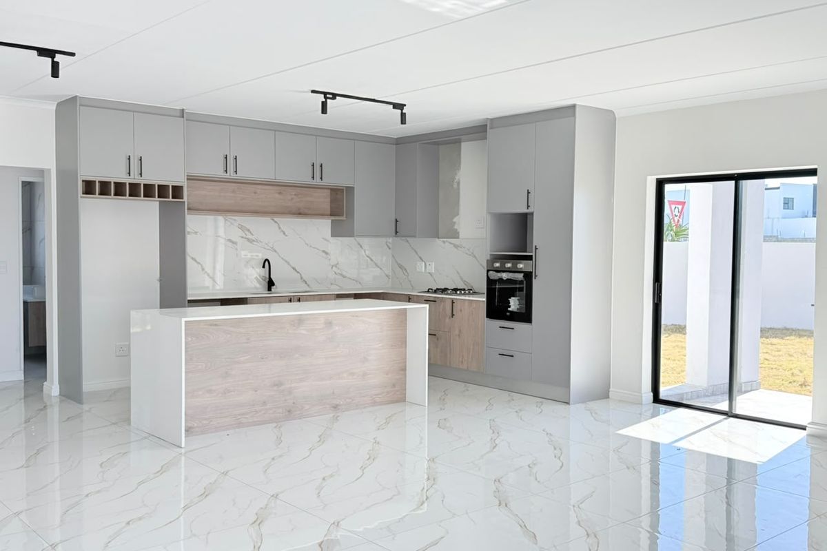 Modern open-plan kitchen featuring sleek grey and wood-tone cabinetry, marble-look splashback, built-in oven, and polished porcelain floor tiles with direct access to the patio.