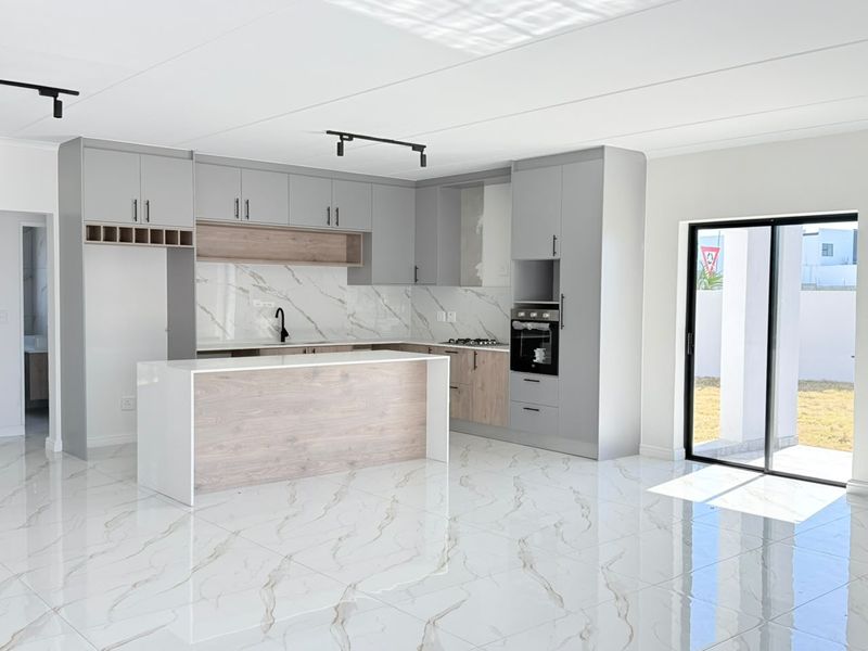 Modern open-plan kitchen featuring sleek grey and wood-tone cabinetry, marble-look splashback, built-in oven, and polished porcelain floor tiles with direct access to the patio.