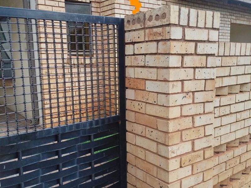 Front entrance view featuring a face brick boundary wall and a black metal security gate.