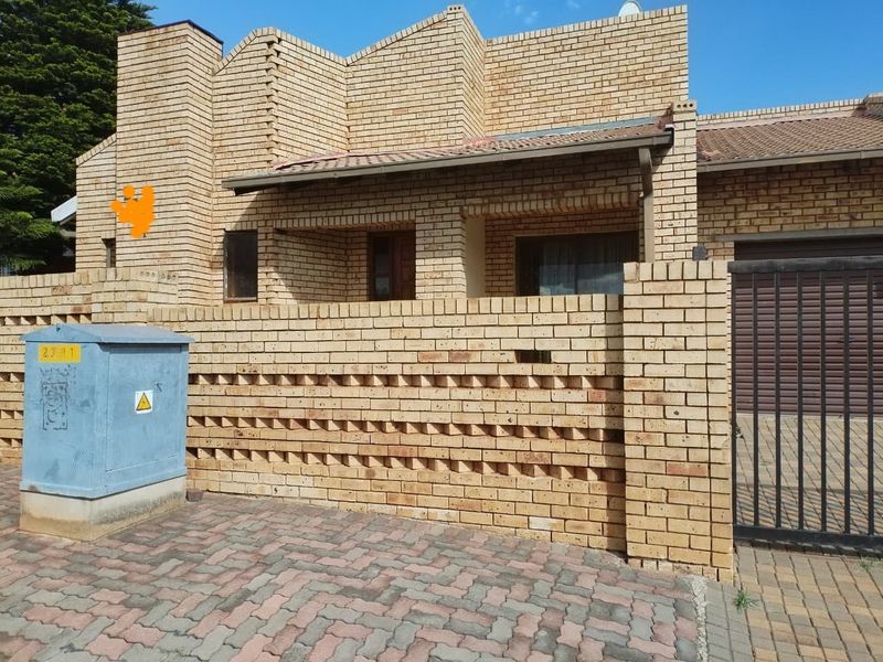 Front elevation of a face brick house featuring a paved driveway, secure metal gate, and a covered entrance porch.