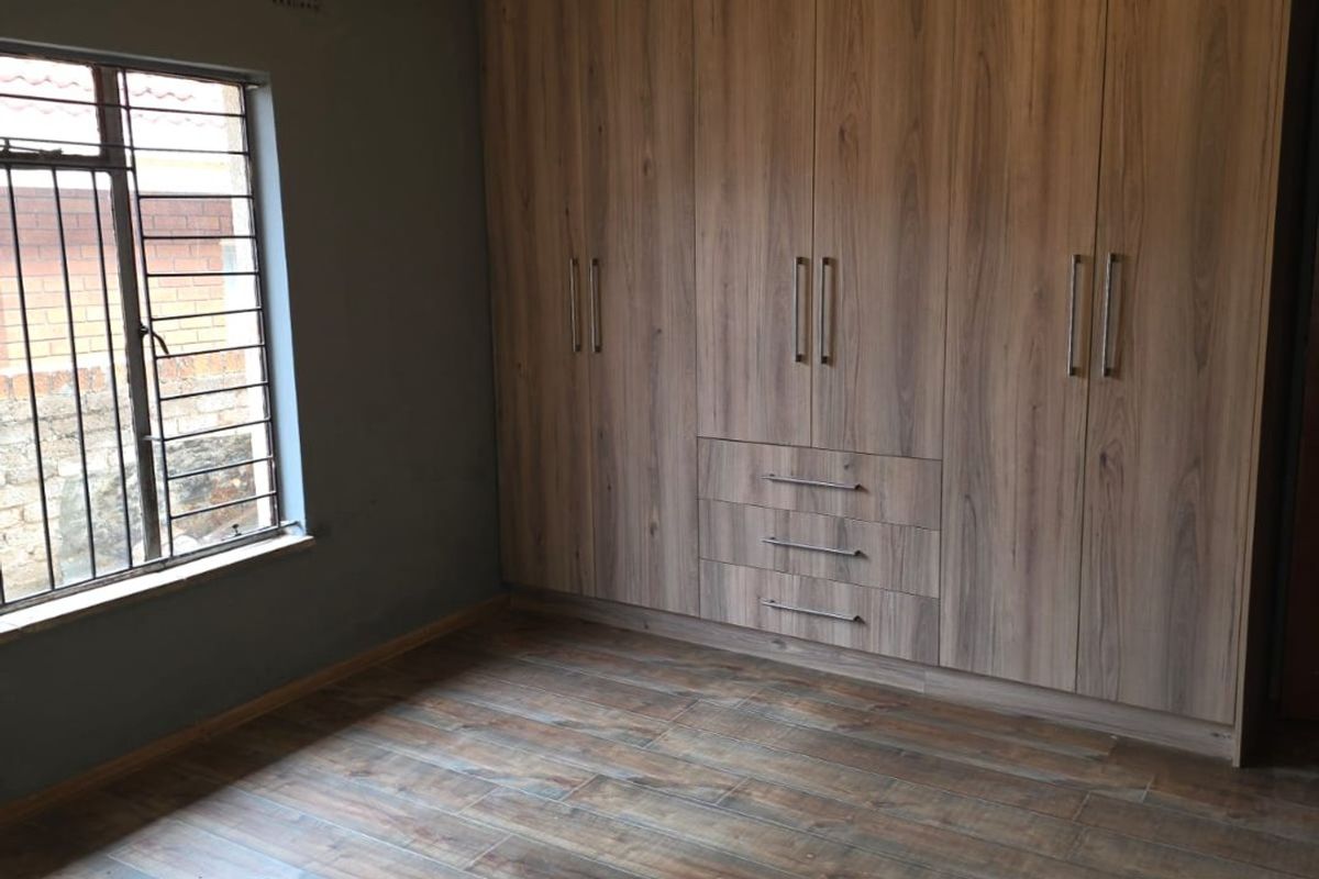 A bedroom featuring wood-look tiled flooring, extensive built-in cupboards, and a window fitted with security burglar bars.