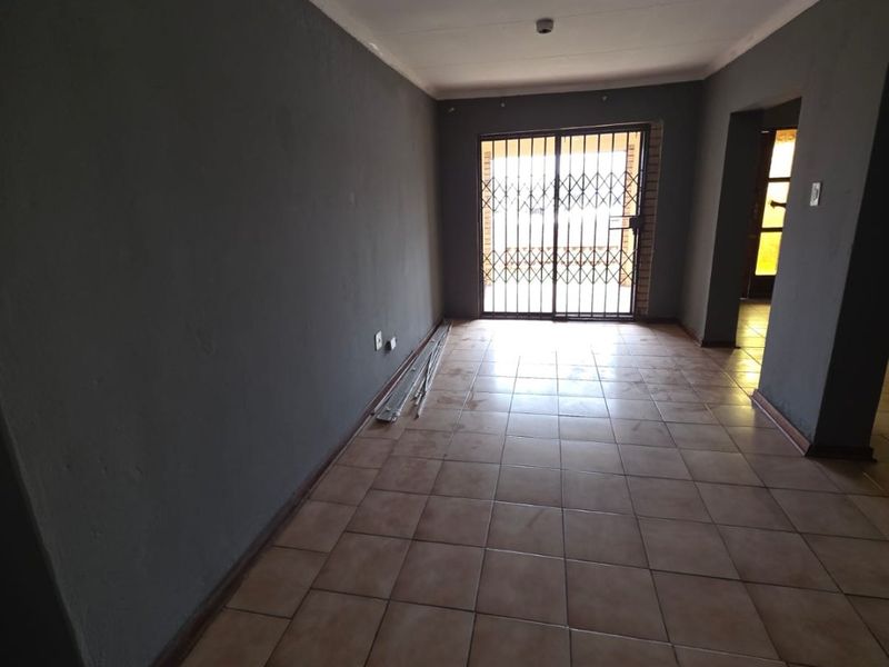 An empty living area featuring tiled flooring, a security gate, and a sliding door leading to the exterior.