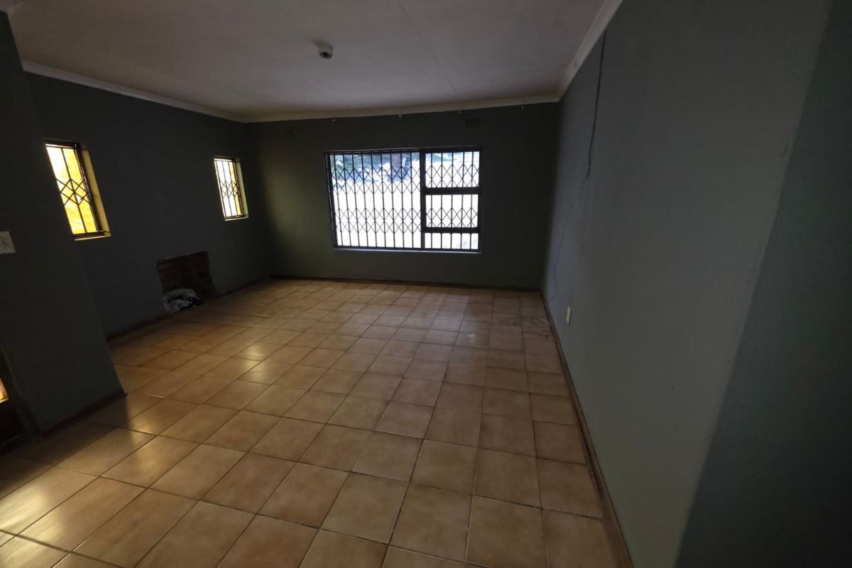 An empty living room featuring tiled flooring, security bars on windows, and a recessed fireplace, awaiting personal touches to enhance its appeal.