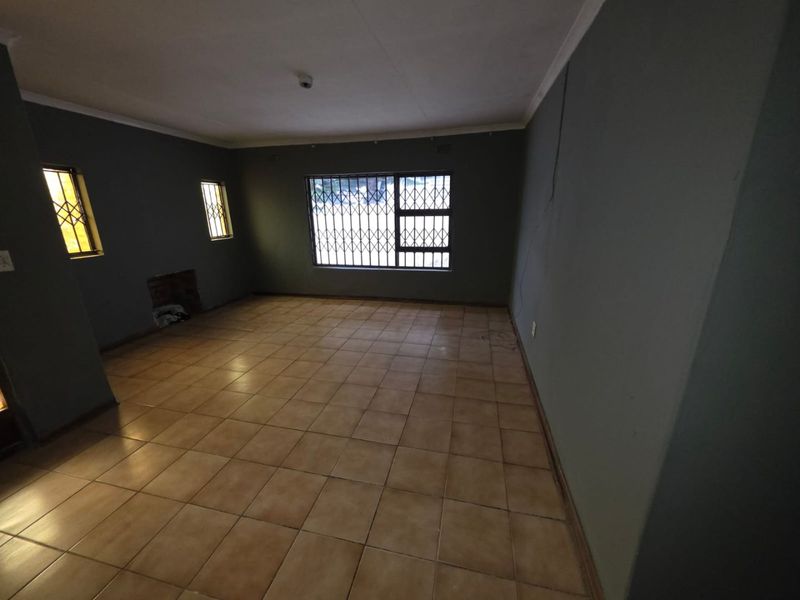 An empty living room featuring tiled flooring, security bars on windows, and a recessed fireplace, awaiting personal touches to enhance its appeal.
