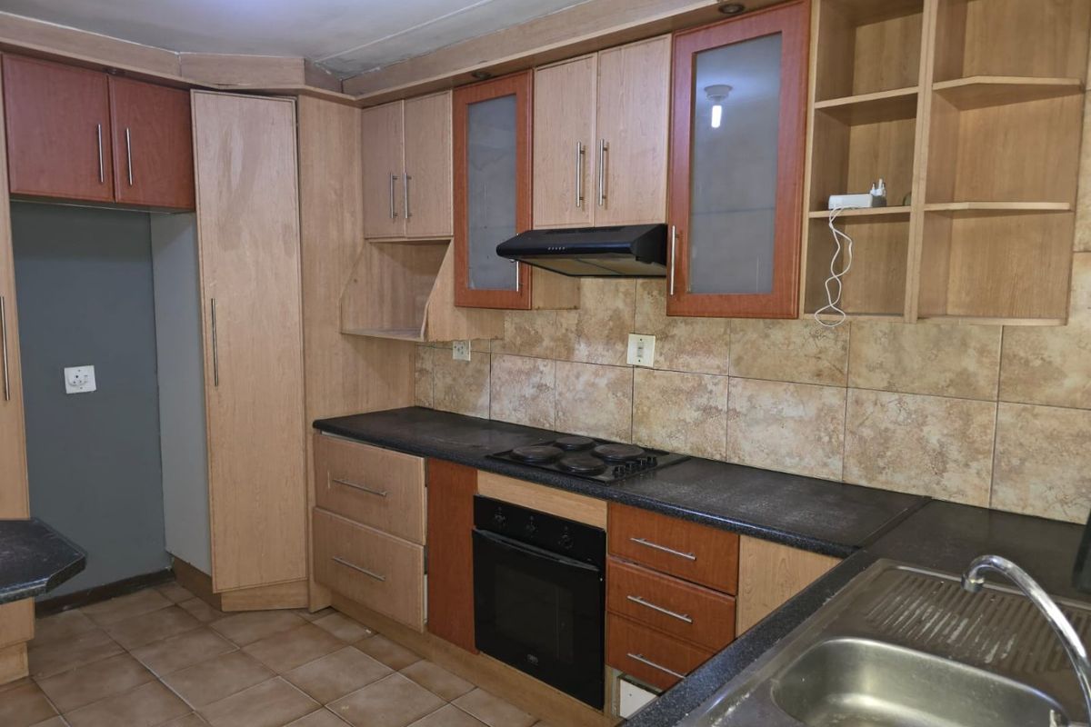 A functional kitchen featuring built-in wooden cabinetry, dark laminate countertops, an integrated oven and hob, and a double bowl stainless steel sink.