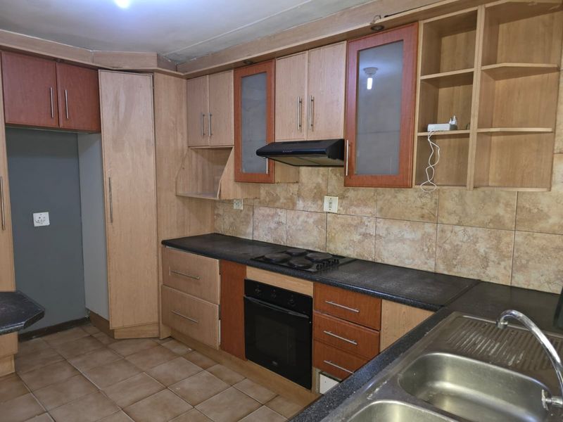 A functional kitchen featuring built-in wooden cabinetry, dark laminate countertops, an integrated oven and hob, and a double bowl stainless steel sink.