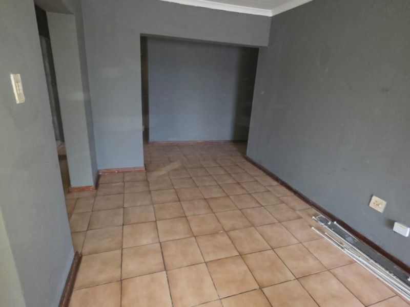 An empty living room featuring ceramic floor tiles, grey painted walls, and coved ceilings, offering a blank canvas for interior design.