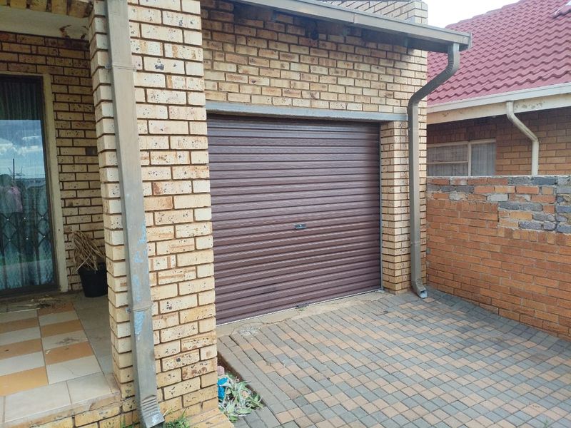 A single garage featuring a brown roller door, brick exterior construction, and a paved driveway area.