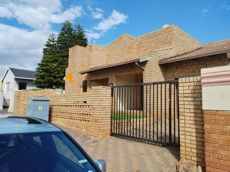 Front elevation of a face brick house featuring a paved driveway, secure metal gate, and a covered entrance area.