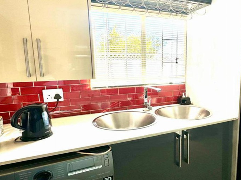 A functional scullery area featuring a double stainless steel sink, modern cabinetry, and a vibrant red subway tile backsplash.