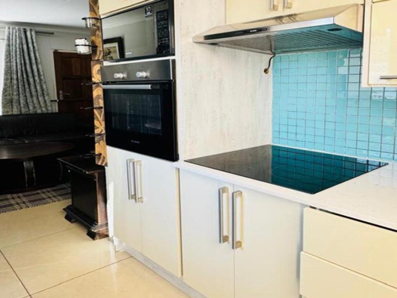 Open plan kitchen area featuring modern fitted cabinetry, stone countertops, built-in oven, microwave, and a vibrant tiled splashback, seamlessly connecting to the living space.