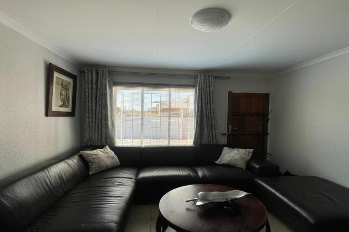 A comfortable living room featuring tiled flooring, a ceiling light fixture, and a window with venetian blinds, providing a functional and well-lit space.