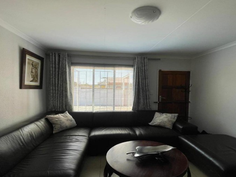 A comfortable living room featuring tiled flooring, a ceiling light fixture, and a window with venetian blinds, providing a functional and well-lit space.