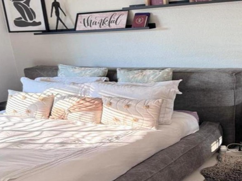 A cozy bedroom featuring a modern upholstered bed frame and minimalist floating wall shelves for display.