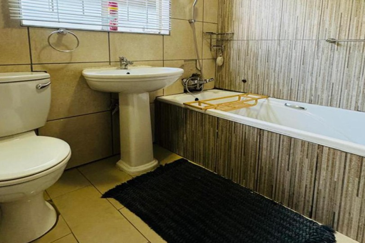 A functional bathroom featuring a pedestal washbasin, a bathtub with shower mixer, and tiled wall finishes.