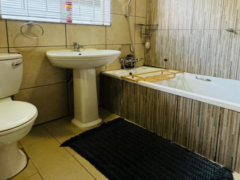 A functional bathroom featuring a pedestal washbasin, a bathtub with shower mixer, and tiled wall finishes.