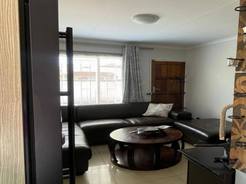 Open plan living area featuring tiled flooring, built-in kitchen appliances, and natural light through a window with security bars.